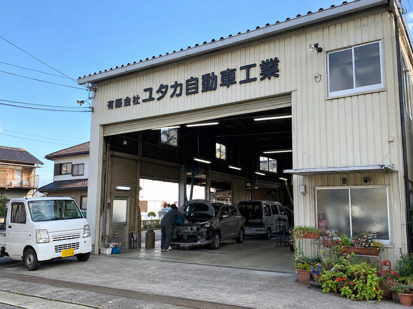 ユタカ自動車工業の社屋外観。ファサードに社名看板、開いたシャッターから作業場が見える