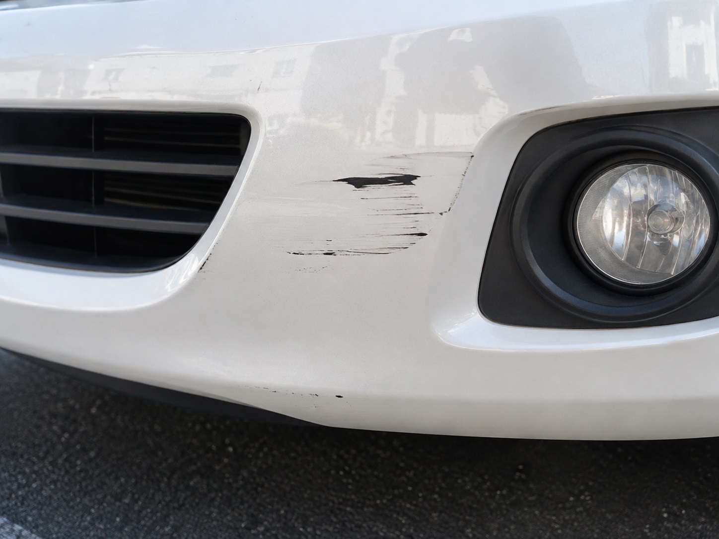 白い車の前バンパーに付いた擦り傷のクローズアップ